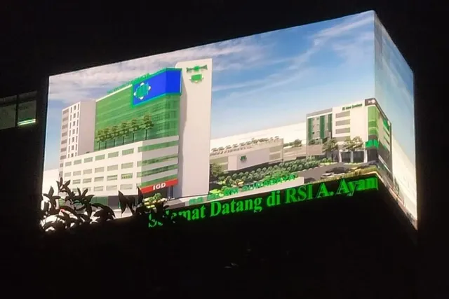 Videotron fasad di sudut gedung Rumah Sakit Islam A. Yani Surabaya menayangkan visual gedung rumah sakit pada malam hari