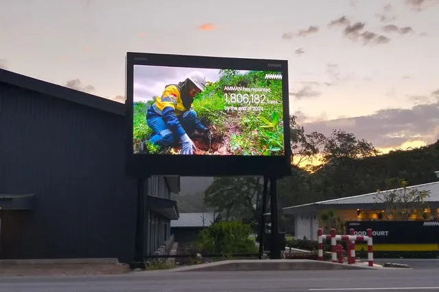 Videotron outdoor P3.9 di atas tiang ganda dalam kawasan industri Nusa Tenggara Barat, menayangkan konten reboisasi saat senja