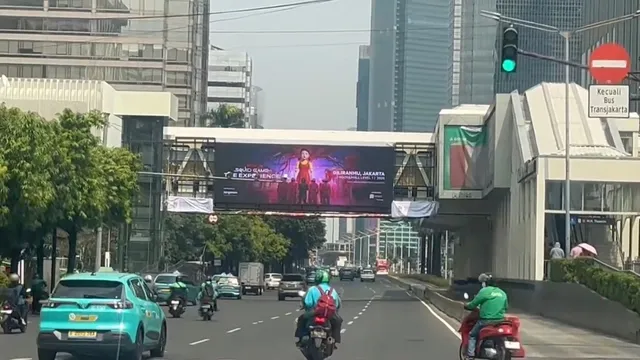 LED bando halte Transjakarta M.H. Thamrin menayangkan poster konser, dengan gedung perkantoran Jakarta di latar belakang