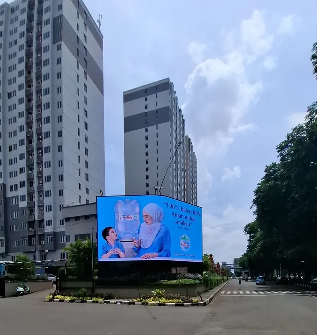 Videotron WGP Kelapa Gading dilihat dari kejauhan di tengah bundaran, dengan apartemen tinggi di latar belakang